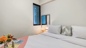 A hotel room with a bed, a nightstand with a lamp, a vase with flowers, and a framed picture on the nightstand. - Well Furnished And Comfort 2Br Meikarta Apartment (Cikarang)