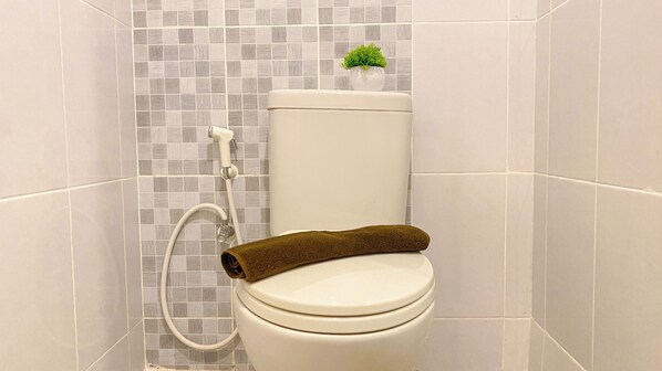 A bathroom with a toilet, a shower, and a small potted plant on the toilet tank.