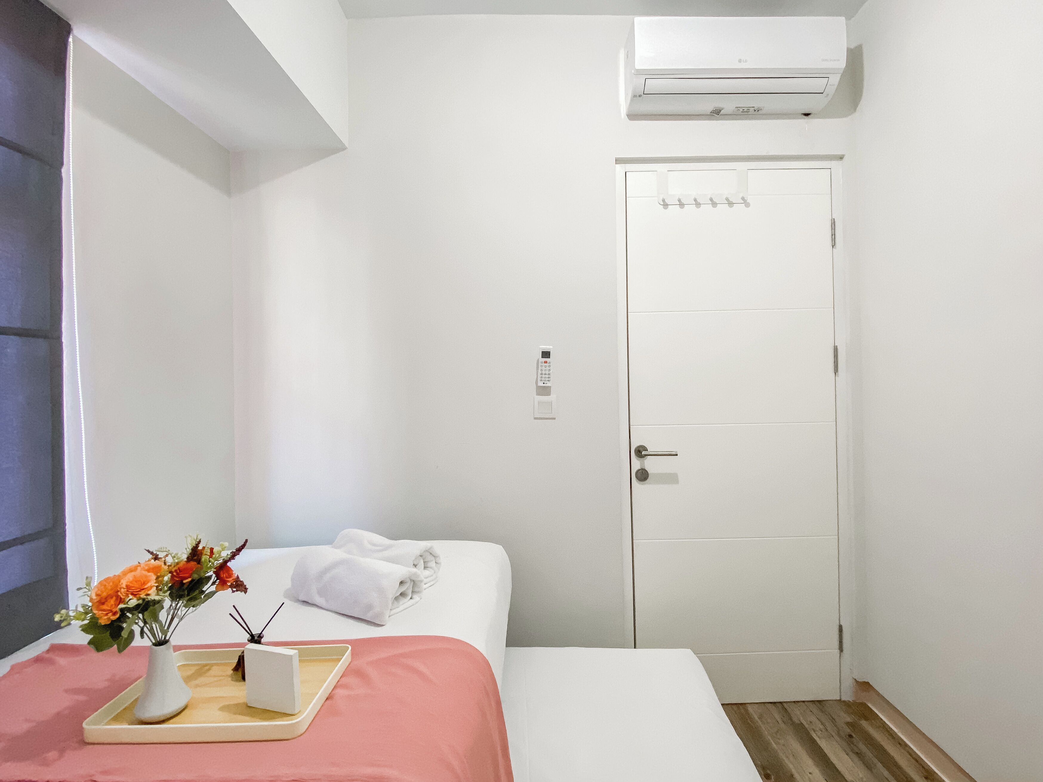Una camera d'albergo con un letto, un comodino con un vassoio, un vaso con fiori e una porta bianca con lettore di badge.