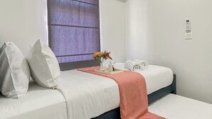 Un lit bien fait, avec des oreillers, une serviette pliée, un vase de fleurs et un magazine posés sur une table de chevet, dans une chambre d’hôtel.