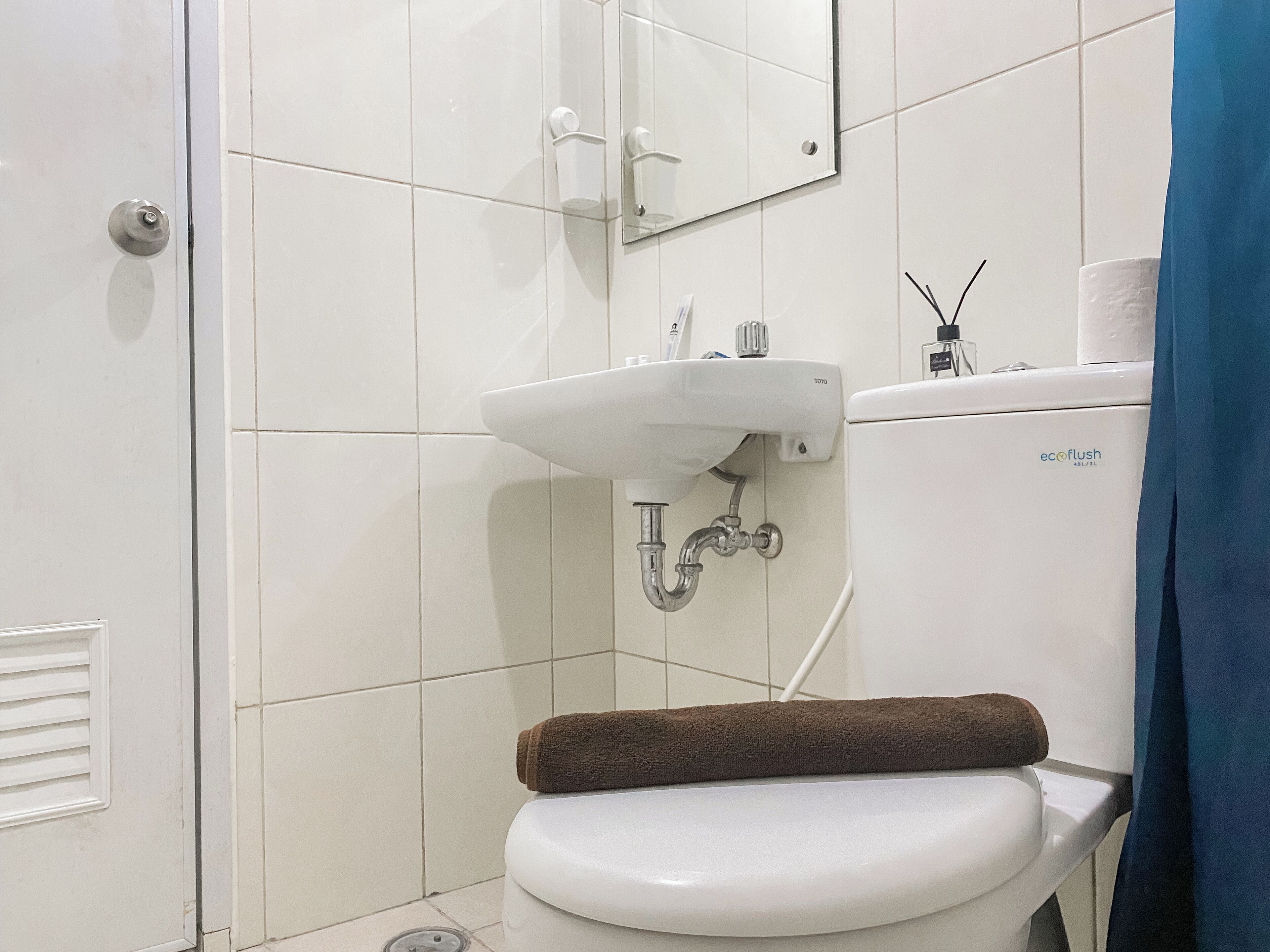 A bathroom with a white toilet, a sink with a mirror above it, and a towel on the toilet seat.