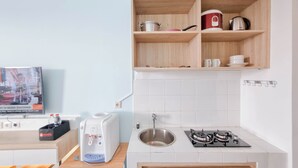 Une cuisine moderne équipée d’une cuisinière à gaz, d’un évier et d’une machine à café. Des étagères en bois, situées au-dessus du plan de travail, servent à ranger les ustensiles de cuisine.