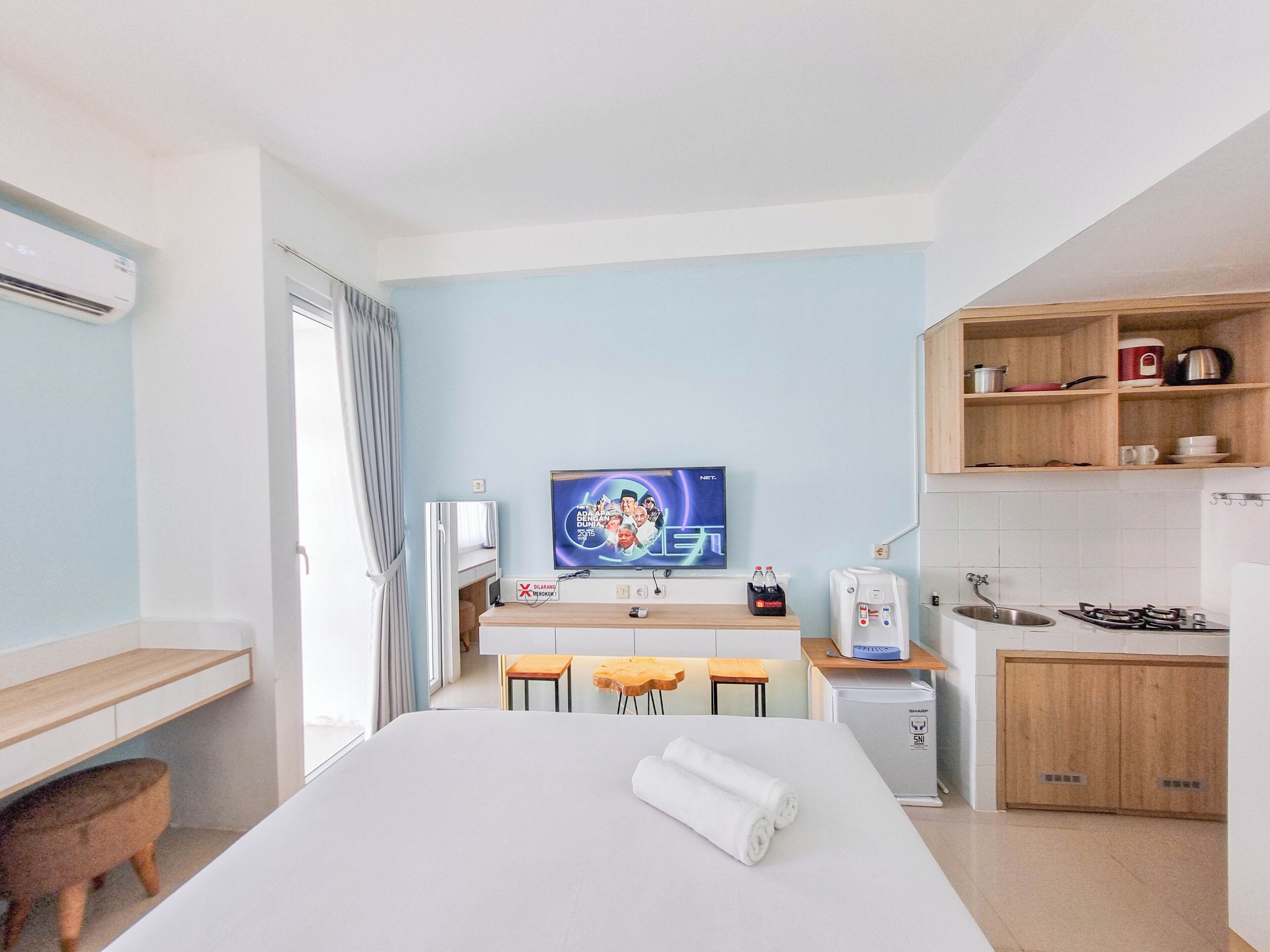 A hotel room with a bed, a TV, a small kitchenette, and a bathroom.