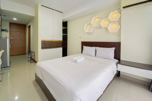 A hotel room with a large bed, a wooden headboard, a bedside table, and hexagonal wall sconces. - The Modern Studio Room At Beverly Dago Apartment (Bandung)
