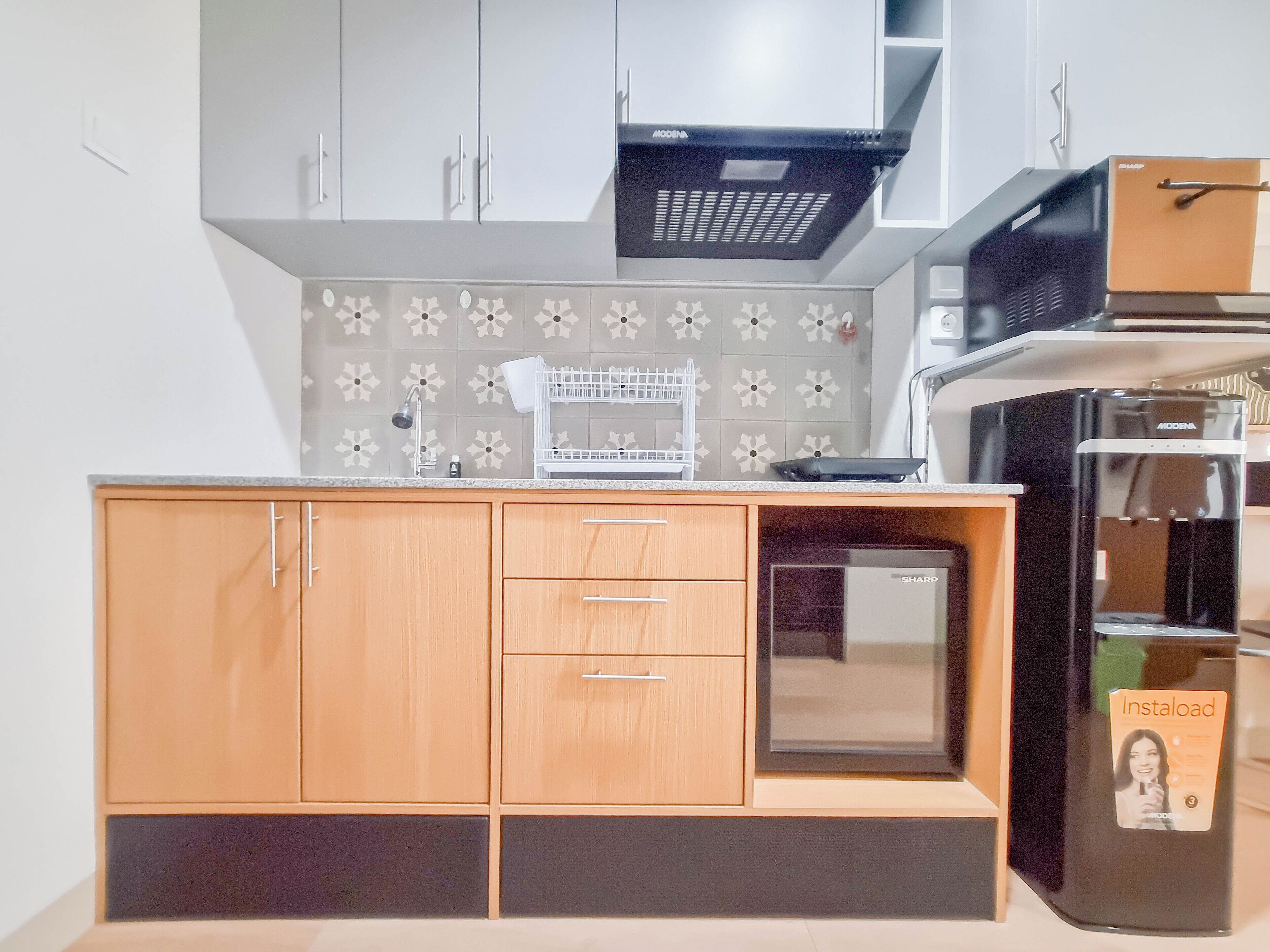 A compact kitchen with white cabinets, a microwave, a refrigerator, and a small countertop with a dish rack.