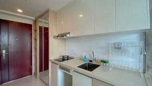 A modern kitchen with a built-in stove, sink, and a wire rack for utensils. - Homey And Clean Studio At Sky House Alam Sutera Apartment (Tangerang)