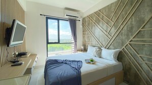 A hotel room with a bed, a TV, a window with curtains, and a view of the city. - Homey And Clean Studio At Sky House Alam Sutera Apartment (Tangerang)