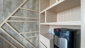 A modern kitchen with a built-in water dispenser, wooden cabinets, and a concrete accent wall. - Homey And Clean Studio At Sky House Alam Sutera Apartment (Tangerang)