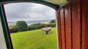 A view through a doorway to a grassy area with a stone well, a red door, and a body of water in the distance. - Unique beachfront cottage at Fintra Bay Donegal (Killybegs)
