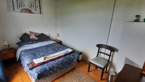 A bedroom with a bed, bedside tables, a chair, a wall-mounted shelf, and a painting. - Unique beachfront cottage at Fintra Bay Donegal (Killybegs)