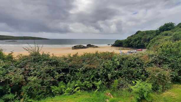A beach with a rocky outcrop, dense greenery, and a cloudy sky. - Unique beachfront cottage at Fintra Bay Donegal (Killybegs)