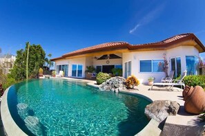 A house with a swimming pool, a patio with lounge chairs, and a garden with rocks and plants. - Luxury Villa | Infinity Pool & Ocean Views (Playa Potrero)