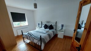 Ein Schlafzimmer mit einem Metallbettgestell, einem Nachttisch mit Lampe, einem Fenster mit Jalousie und einem Holzboden.