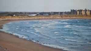Ein Strand mit Wellen, sandigem Ufer und Gebäuden im Hintergrund.