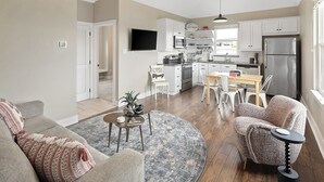 A modern kitchen with white cabinets, a stainless steel refrigerator, and a flat-screen TV mounted above the counter. - Luxury Apartment | Pvt. Parking | @ Kyle Field (College Station)
