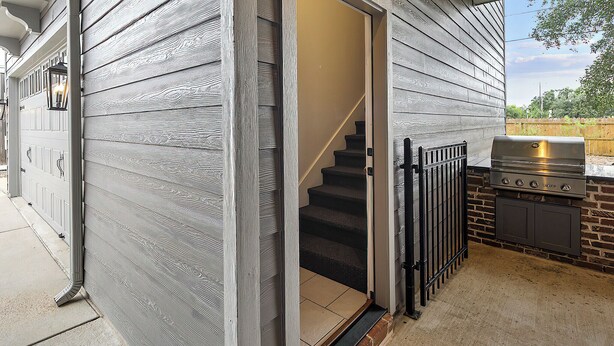 A house with a gray exterior, a wooden staircase, and a barbecue area with a grill. - Luxury Apartment | Pvt. Parking | @ Kyle Field (College Station)