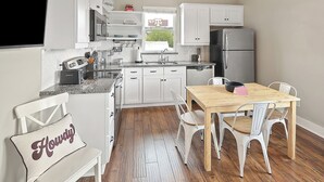 A compact kitchen with white cabinetry, a wooden dining table, and a bench with a pillow. - Luxury Apartment | Pvt. Parking | @ Kyle Field (College Station)