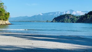 A beach with clear blue water, a sandy shore, and a mountain range in the background. - Casa Amable by Ronny's place - Manuel Antonio (Quepos)