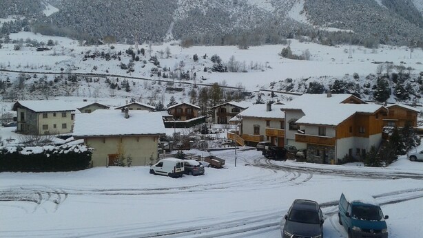 Un pueblo cubierto de nieve con casas, un camino sinuoso y una montaña al fondo.