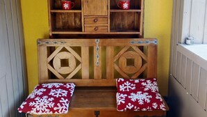 Un rincón acogedor con un banco y una mesa de madera, con un aparador con forma de corazón arriba y dos cojines rojos con copos de nieve blancos.