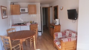 Una cocina compacta con armarios de madera, microondas y cafetera. Hay una mesa de comedor con sillas y un sofá en la sala de estar.