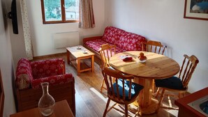 Una habitación acogedora con un sofá rojo estampado, una mesa de comedor de madera y sillas. Hay una ventana con cortinas, un radiador y un aplique de pared.