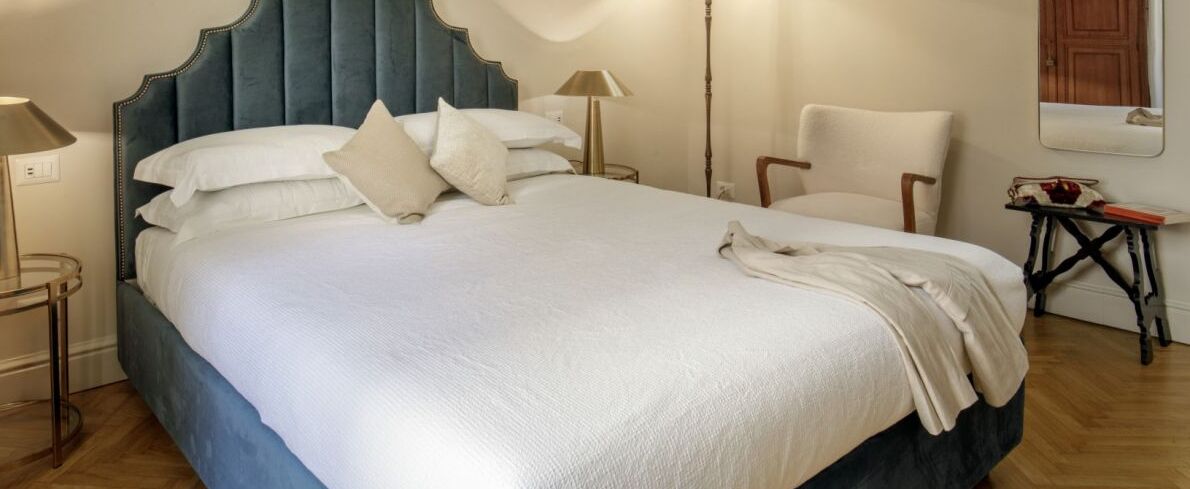 A neatly made bed with a blue headboard, white bedding, and a small bedside table with a lamp.
