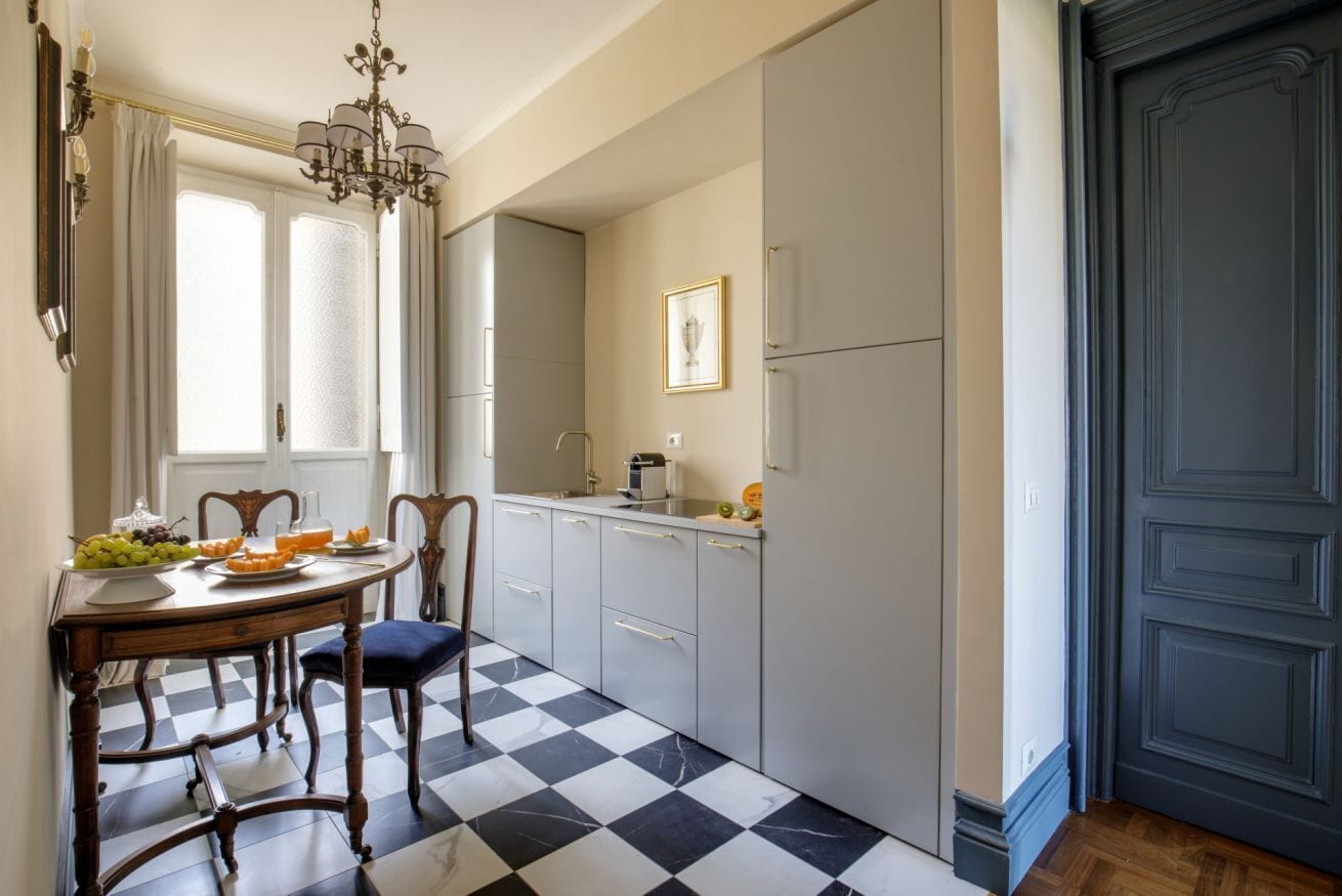 A kitchen with a checkered floor, a dining table with chairs, a chandelier, and a refrigerator.