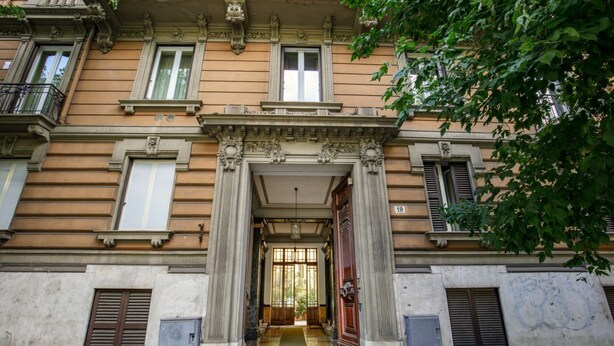 Une façade d’immeuble avec une entrée centrale, de grandes fenêtres et un balcon.