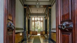 Un vaste hall d’entrée orné de portes en bois sculpté, doté d’un sol en marbre et surmonté d’un lustre.