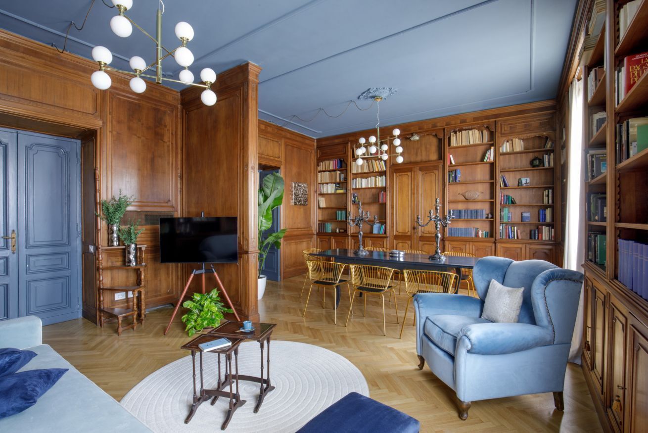 Un salon spacieux doté d’un plancher en bois, d’un canapé bleu, d’une table à manger avec des chaises et d’une bibliothèque remplie de livres.