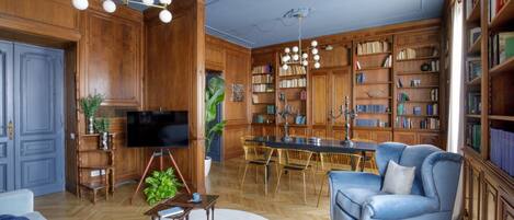 Un salon spacieux doté d’un plancher en bois, d’un canapé bleu, d’une table à manger avec des chaises et d’une bibliothèque remplie de livres.