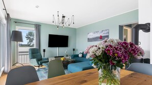 A modern living room with a sofa, a TV, and a vase of flowers on a wooden table. - Beautiful apartment in Olpenitz (Olpenitz)