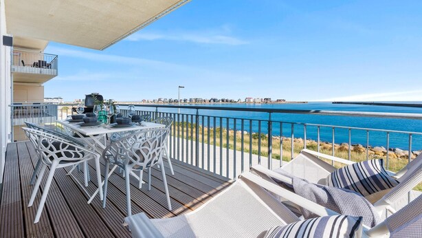 A balcony with a table set for dining, overlooking a coastal view with a clear sky. - Beautiful apartment in Olpenitz (Olpenitz)