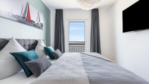 A bedroom with a bed, pillows, a painting, a TV, and a balcony view. - Beautiful apartment in Olpenitz (Olpenitz)