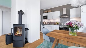 A modern kitchen with a wood-burning stove, white cabinets, and a dining area with a wooden table and chairs. - Beautiful apartment in Olpenitz (Olpenitz)