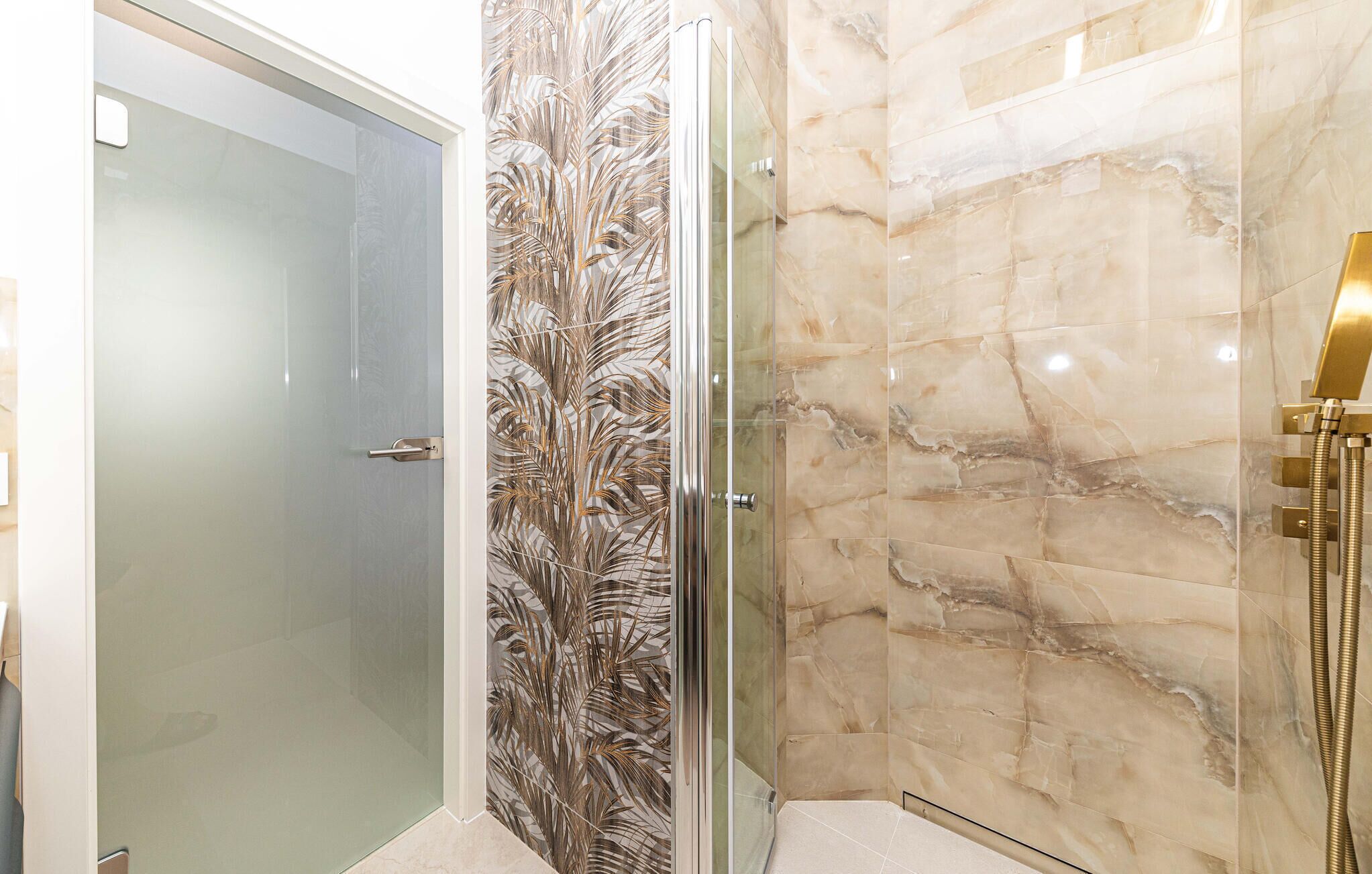 A modern bathroom with a glass shower enclosure, a marble wall, and a gold showerhead.