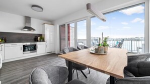 Une cuisine moderne avec des meubles blancs, un four encastré et une grande fenêtre donnant sur une marina.
