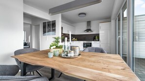 Une cuisine moderne avec des meubles blancs, un four encastré et un coin repas comprenant une table en bois et des chaises grises.