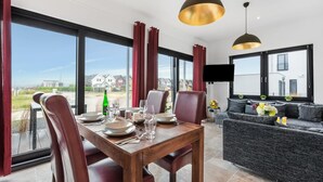Un coin repas avec une table dressée pour quatre personnes, de grandes fenêtres et un canapé en arrière-plan.