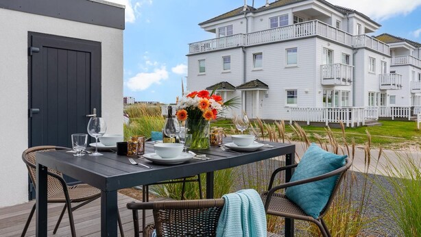 Une table à manger installée à l’extérieur, avec en arrière-plan un immeuble blanc à plusieurs étages.