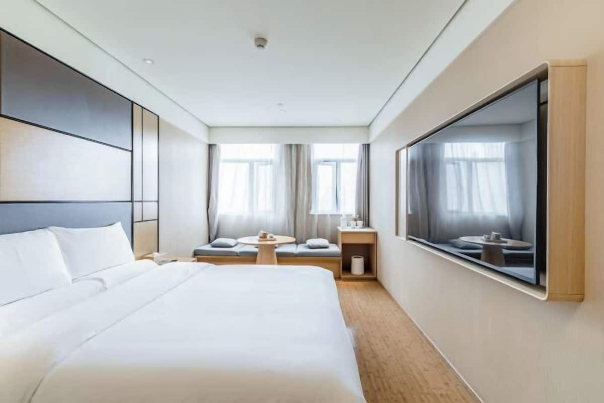 A modern hotel room with a large bed, a seating area with a table, and a large window.