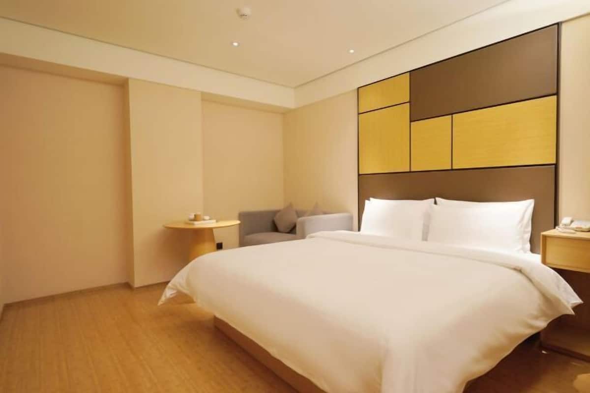 A hotel room with a large bed, a bedside table, a chair, and a nightstand.