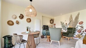 A modern living room with a round wooden table, wicker chairs, a green armchair, and a large wall mural. - Cocon du Clos - PEAULE (PEAULE)