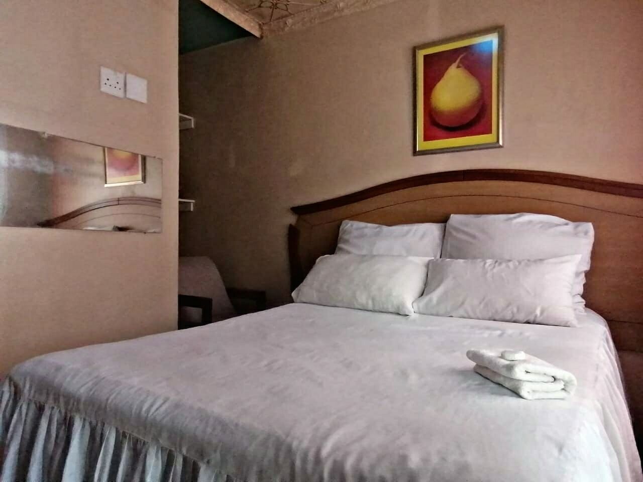 A neatly made bed with white linens and pillows, a framed artwork on the wall, and a folded towel on the bed.