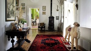 Un intérieur traditionnel avec un tapis rouge à motifs, une table en bois ornée de photos encadrées, une statuette de chien décorative et, au fond, une pièce éclairée de lumière verte.