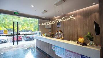 A reception desk with a wooden finish, a digital display, and a view of the street outside.