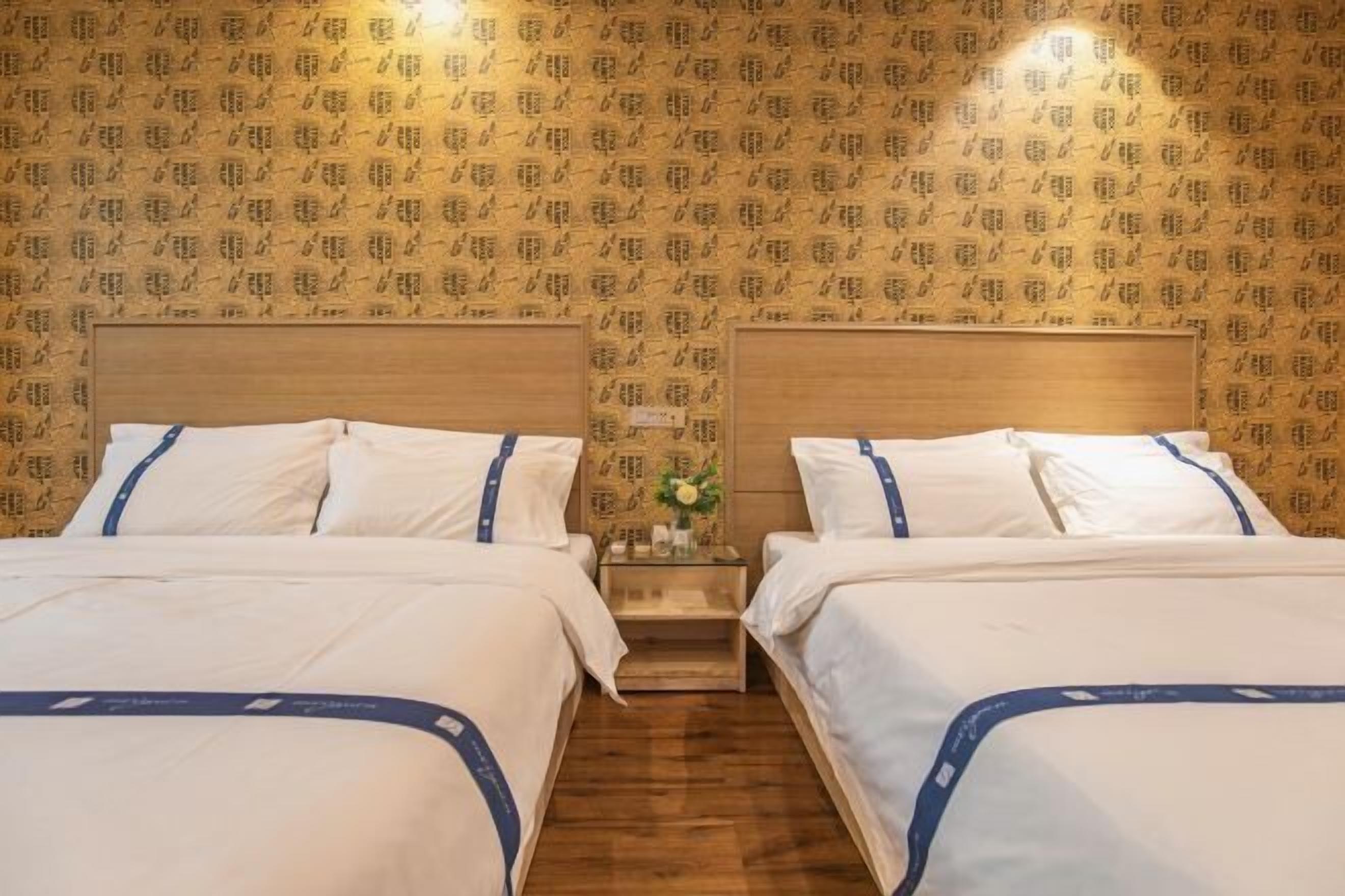 Een hotelkamer met twee bedden, houten hoofdborden en behang met een patroon.