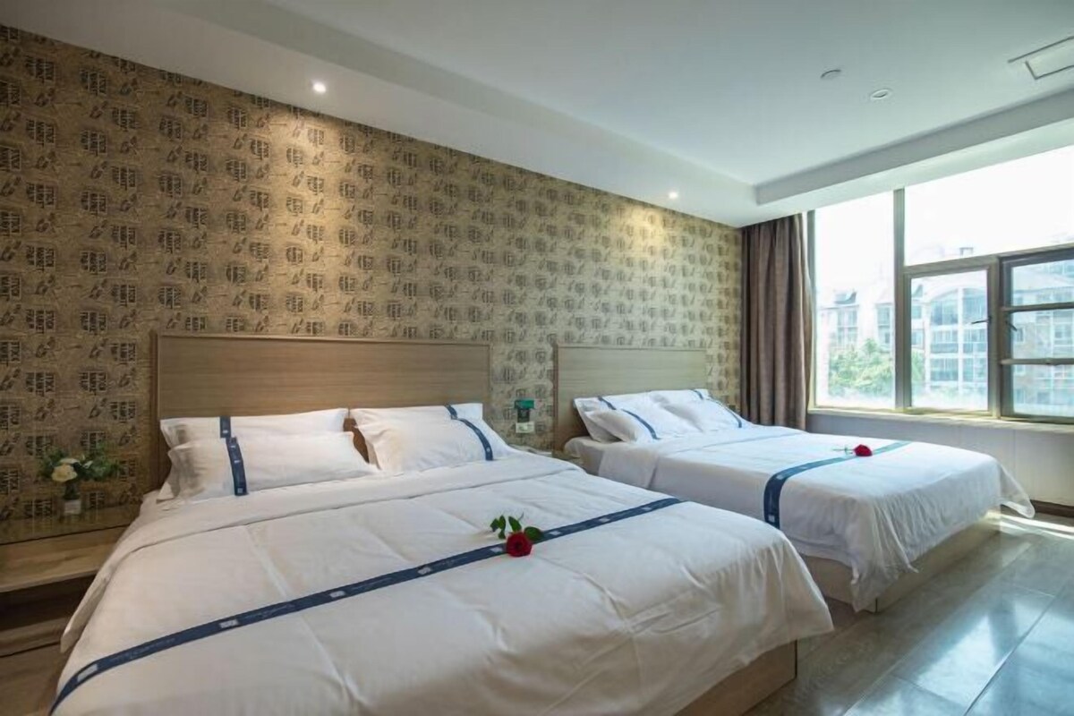 A hotel room with two beds, a large window, and patterned wallpaper.