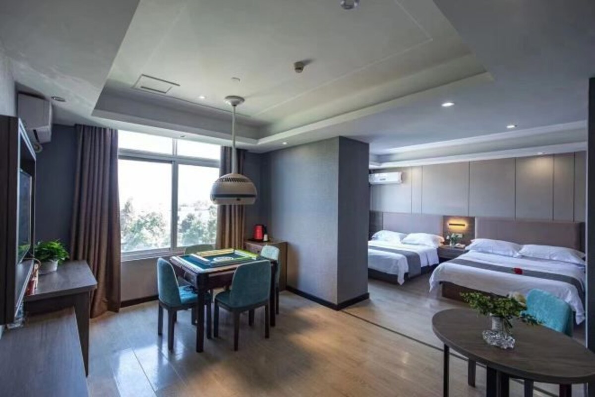A hotel room with a desk, two beds, a dining area, and a large window.